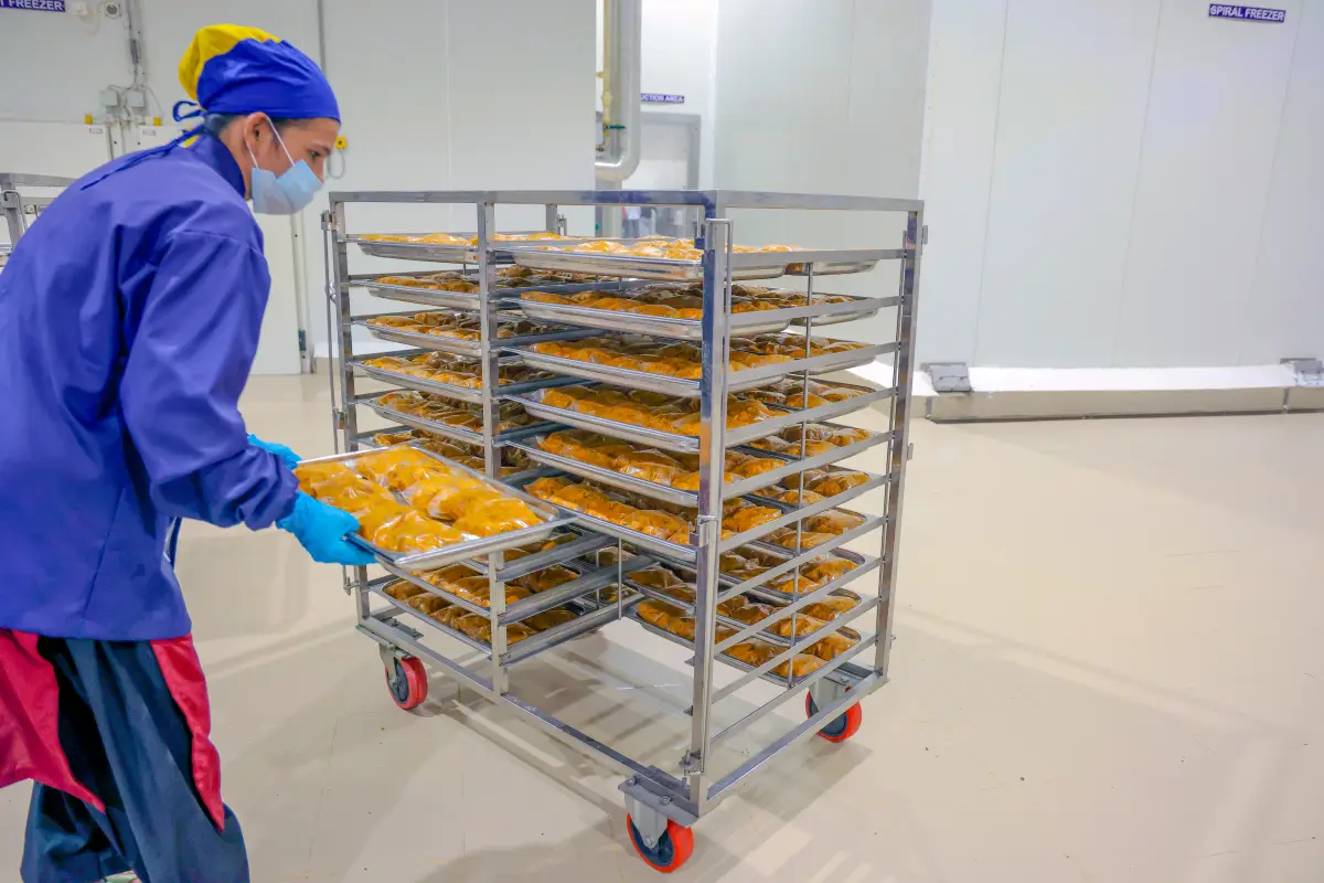 Worker in gloves and a mask loading trays onto a rack at Rudrapur